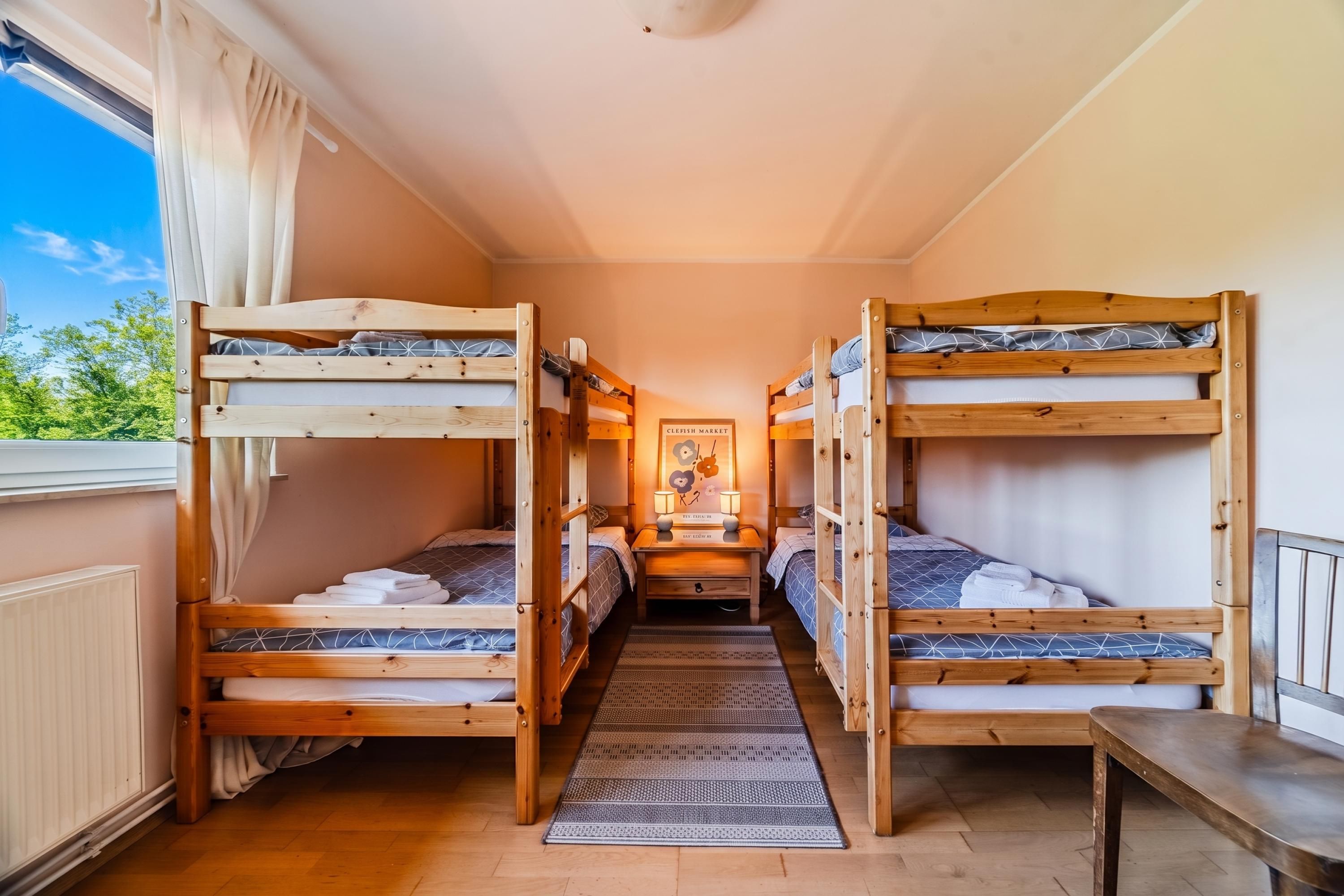 Een kamer met stapelbedden, een raam met gordijnen, een vloerkleed en een bord aan de muur.