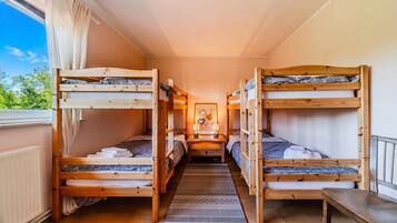 Een kamer met stapelbedden, een raam met gordijnen, een vloerkleed en een bord aan de muur.
