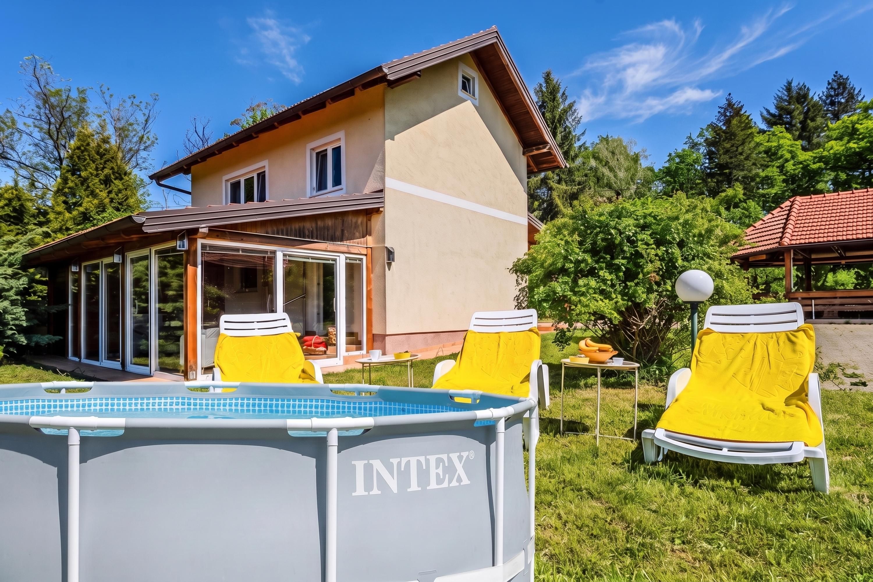 A house with a swimming pool, two yellow lounge chairs, and a covered patio area.