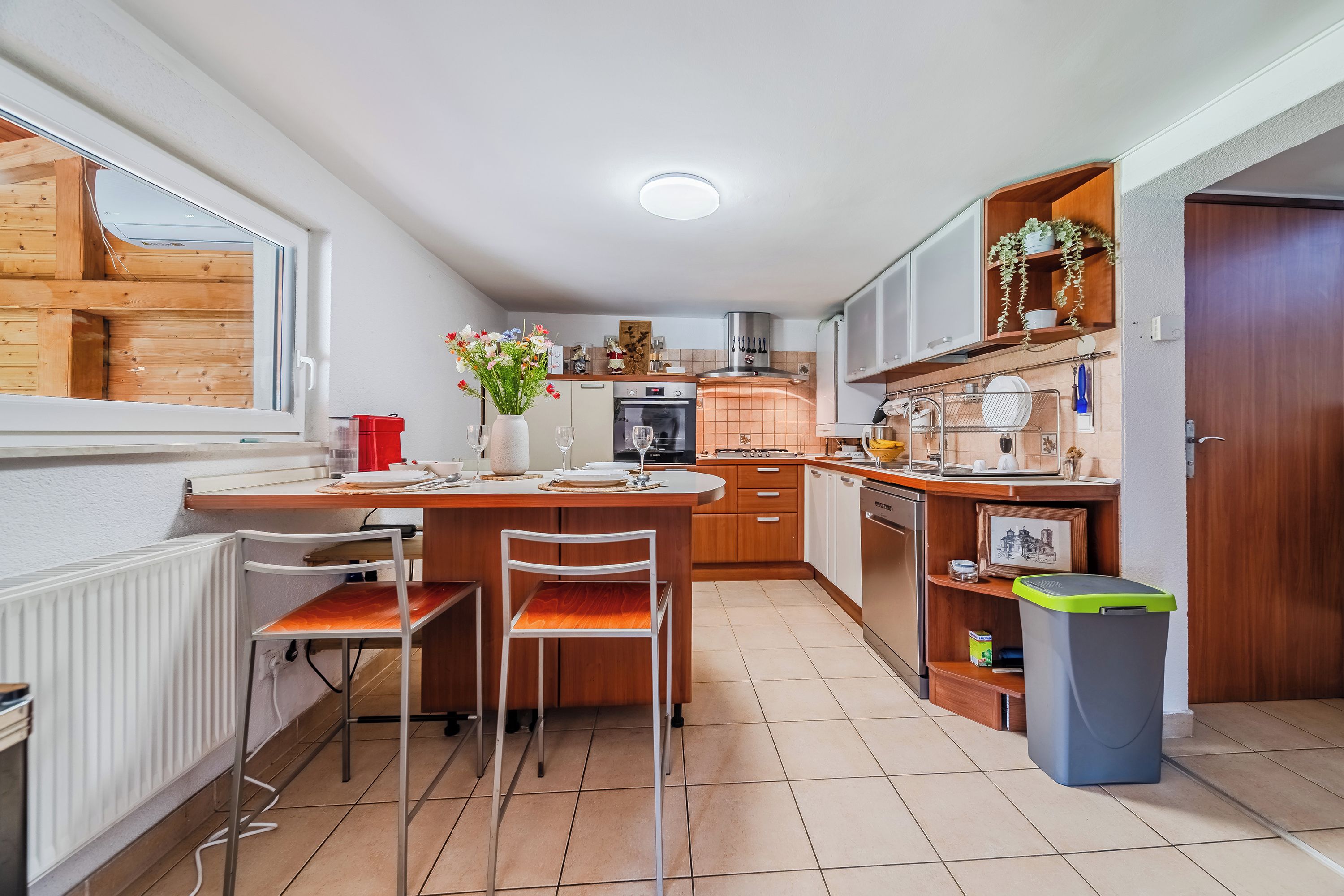 Una cocina compacta con comedor, armarios de madera, horno empotrado y ventana con vistas a una construcción de madera.