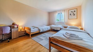 Hotellihuone, jossa on kaksi erillistä sänkyä, työpöytä tuolilla, pieni pöytä lampun kanssa ja ikkuna, jossa on verhot.
