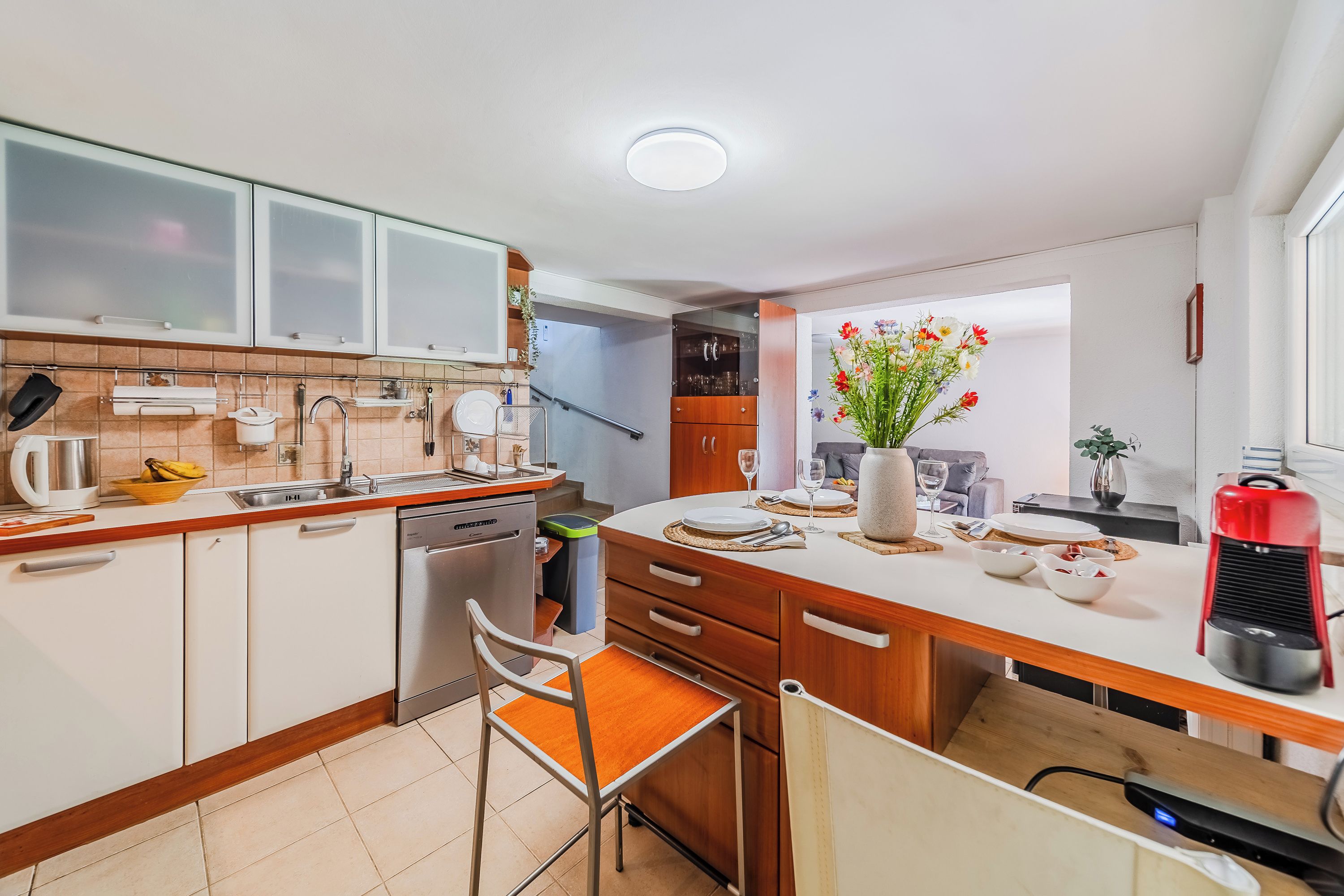 A modern kitchen with white cabinets, a wooden countertop, a built-in oven, and a dining area with a chair and table.