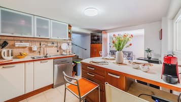 Een moderne keuken met witte kastjes, een houten aanrecht, een inbouwoven en een eethoek met een stoel en tafel.