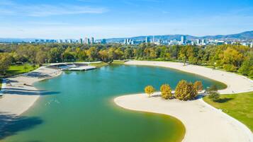An aerial view of a park with a lake, sandy areas, and a cityscape in the background.