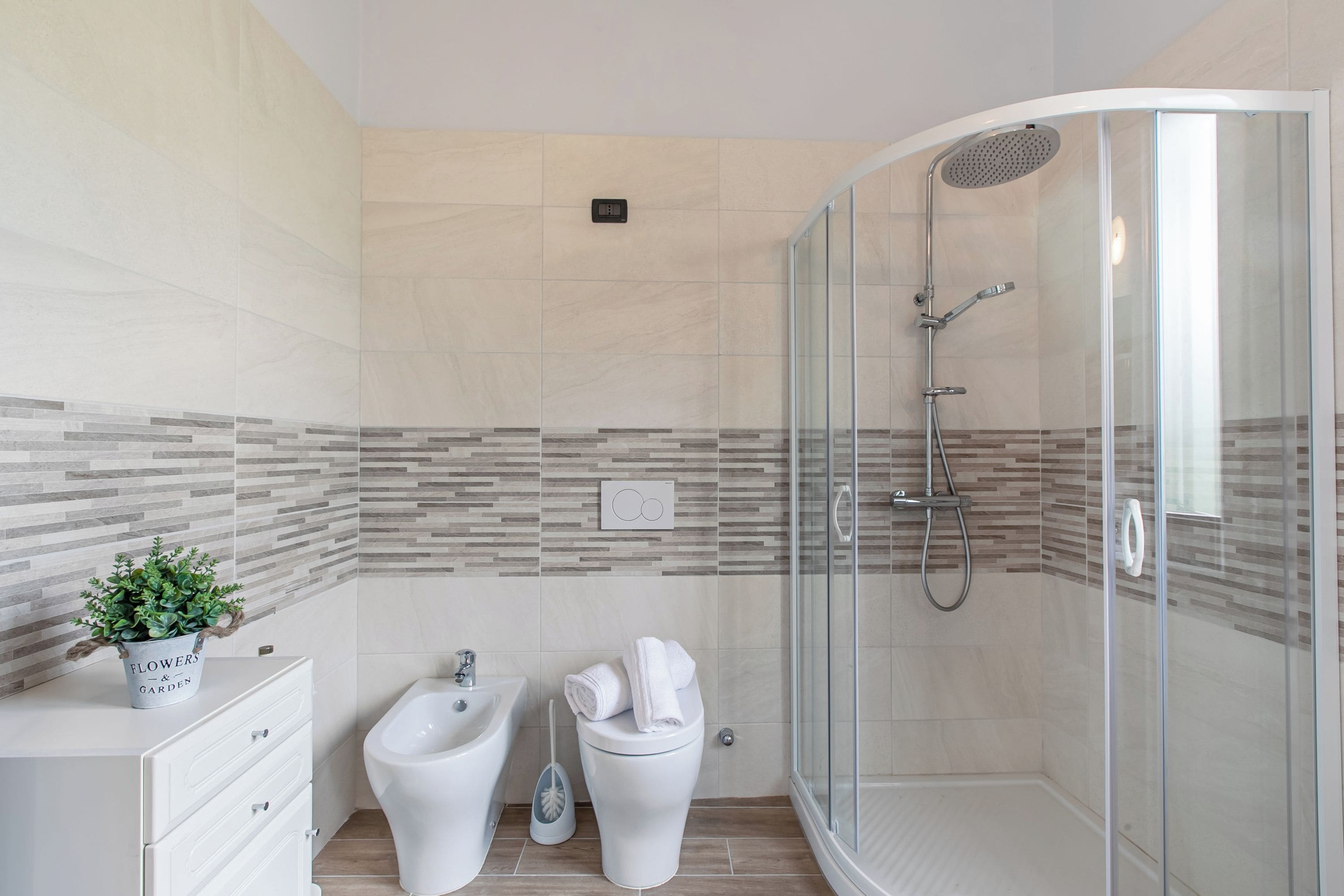 A modern bathroom with a shower, bidet, and a small plant on a cabinet.