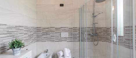 A modern bathroom with a shower, bidet, and a small plant on a cabinet.