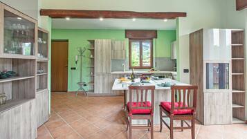 A kitchen with wooden cabinets, a dining area with two chairs, and a window with a view of greenery.
