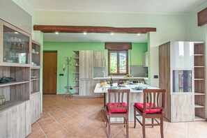 Uma cozinha com armários de madeira, um espaço de jantar com duas cadeiras e uma janela com vista para o verde.