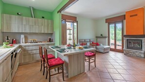 A spacious kitchen with a central island, wooden cabinets, and a dining area with red chairs. - La Dimora Dei Colori Private Garden Near Stresa (Brovello-Carpugnino)