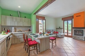 A spacious kitchen with a central island, wooden cabinets, and a dining area with red chairs. - La Dimora Dei Colori Private Garden Near Stresa (Brovello-Carpugnino)