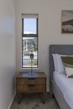 Une chambre à coucher avec un lit, une table de chevet avec une lampe, une fenêtre donnant sur un paysage et un tableau accroché au mur.