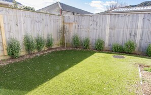 Une cour arrière clôturée avec une pelouse artificielle, une grille de drainage et de petits arbustes le long de la clôture.