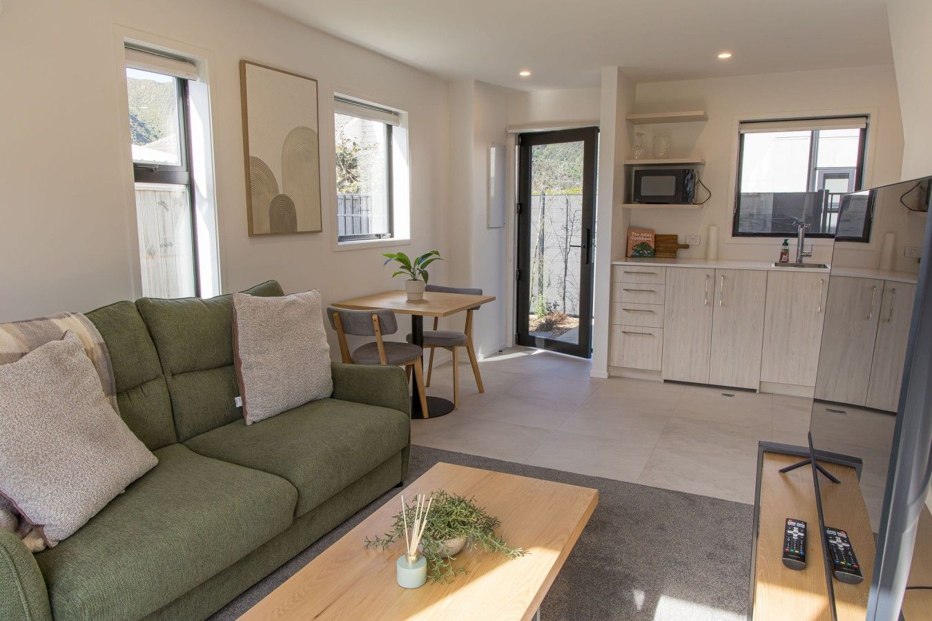 A modern living room with a green sofa, a coffee table, and a dining area with a table and chairs.