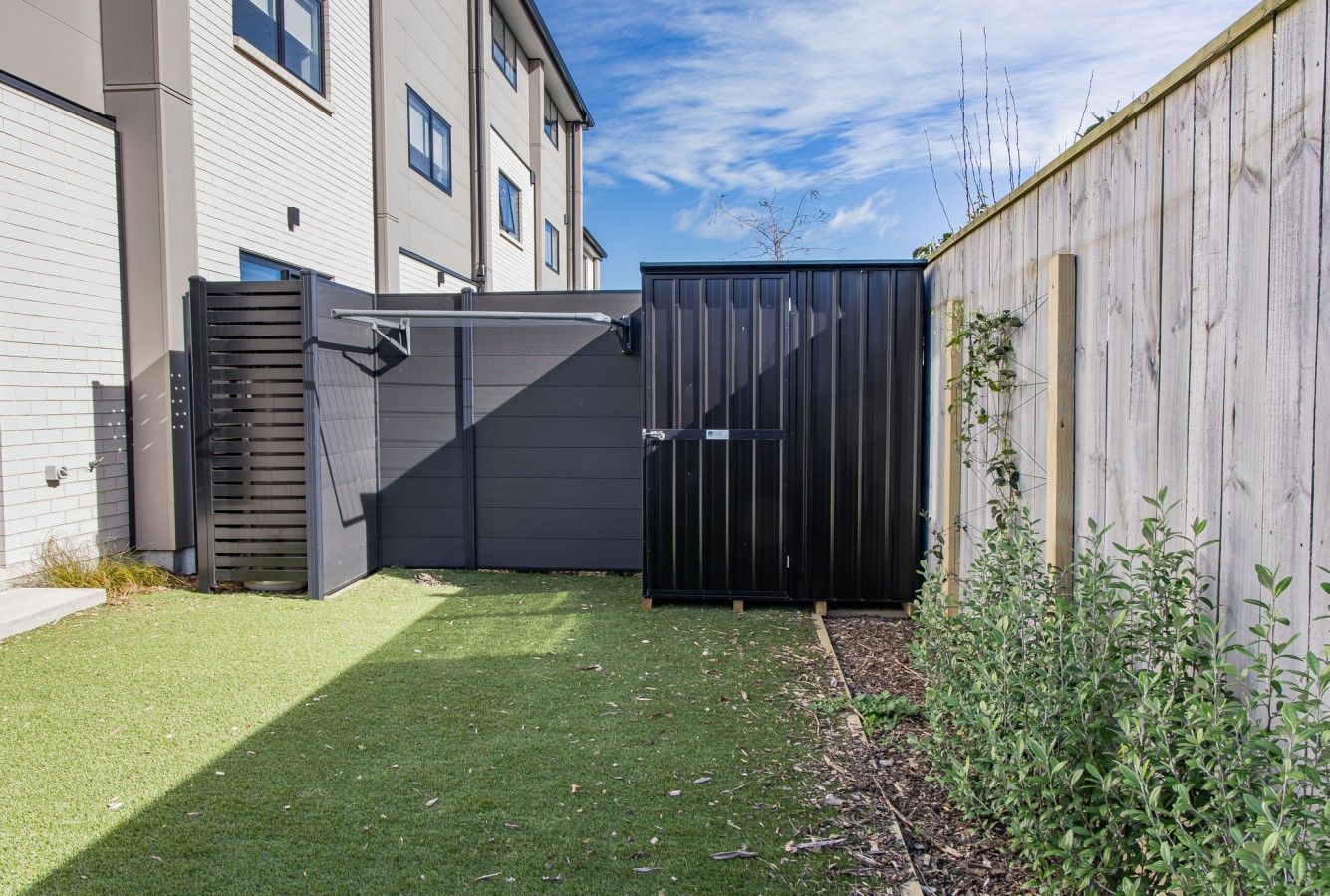A fenced backyard with artificial grass, a wooden fence, and a building with windows.