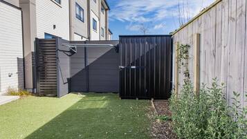 A fenced backyard with artificial grass, a wooden fence, and a building with windows.