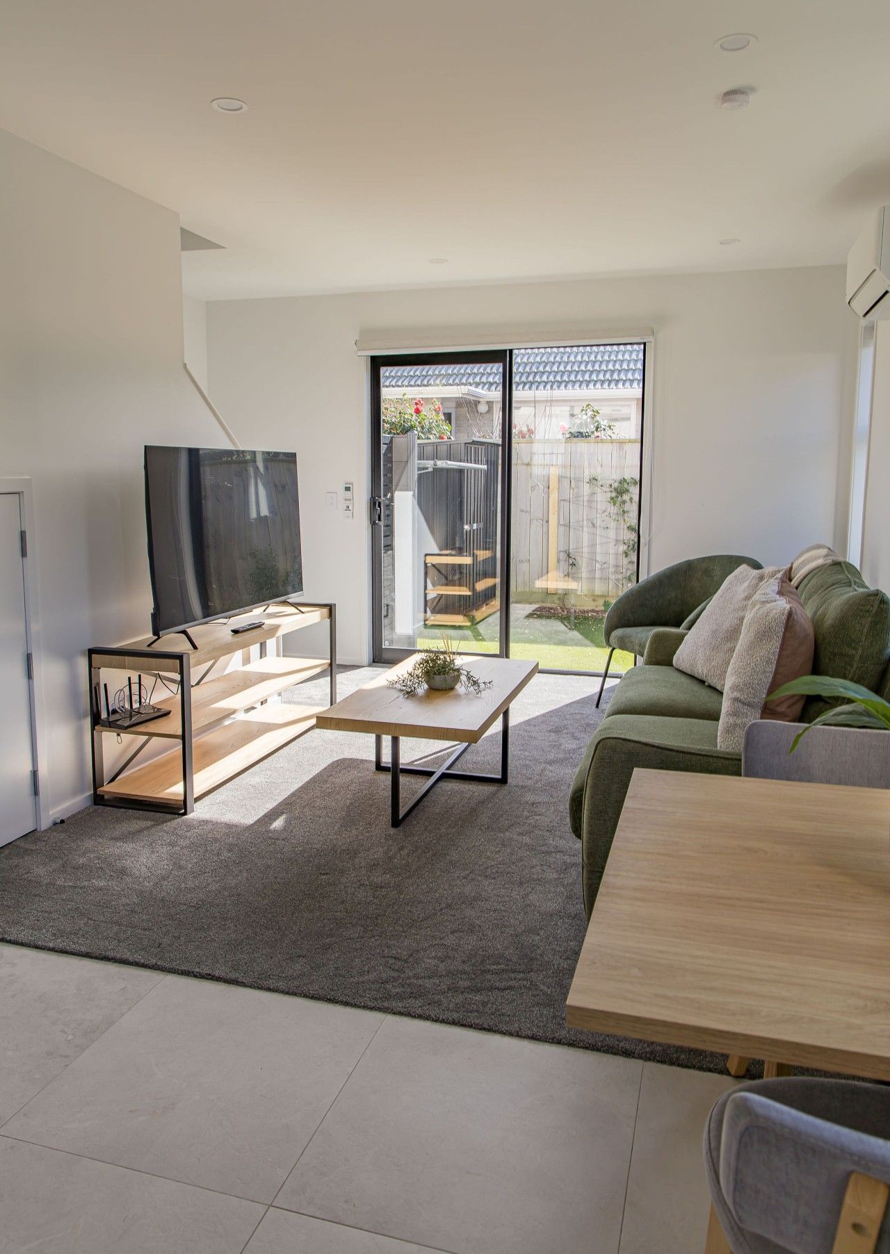 A modern living room with a flat-screen TV, a wooden coffee table, a green sofa, and a dining table.