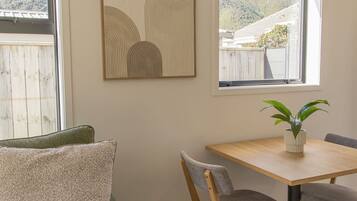 A room with a green sofa, a wooden dining table with two chairs, and a potted plant on the table.