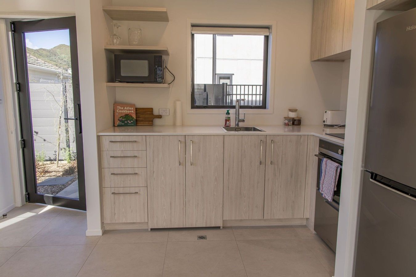 A modern kitchen with a built-in microwave, a window, and a stainless steel refrigerator.