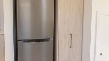 A stainless steel refrigerator with a sticker indicating an energy rating, positioned next to a wooden wardrobe in a room with white walls and a tiled floor.