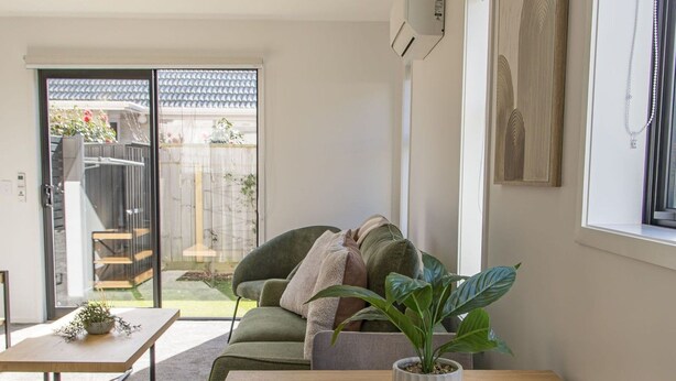 A modern living room with a sofa, a dining table, and a potted plant.