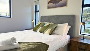 Un lit bien fait, avec des oreillers, une lampe de chevet et une vue sur une montagne par la fenêtre.