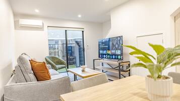 A modern living room with a sofa, armchair, TV, and a dining table.