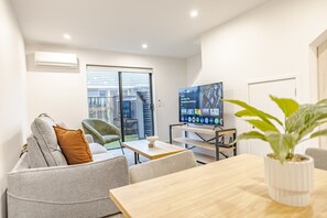A modern living room with a sofa, armchair, TV, and a dining table.