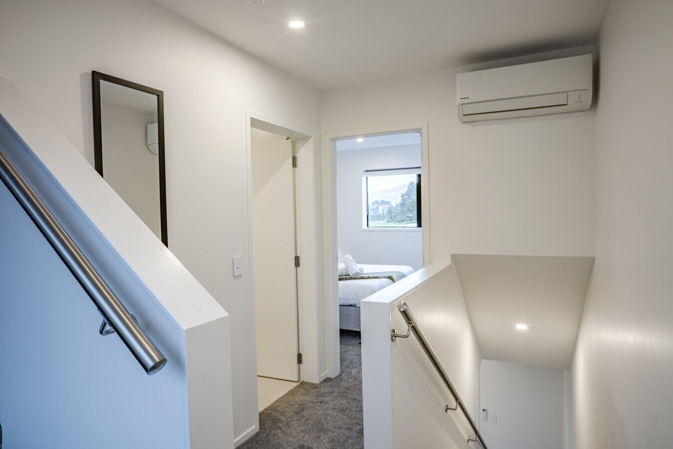 A hallway with a staircase, a door leading to a bedroom, and an air conditioning unit mounted on the wall.