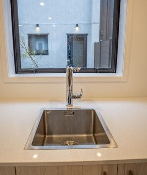 A stainless steel kitchen sink with a modern faucet, a window above it, and a light-colored countertop. - Stylish Two-Bedroom Townhouse Near Lower Hutt (Lower Hutt)