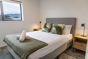 A bedroom with a bed, two bedside tables, a window, and a view of the outside. - Stylish Two-Bedroom Townhouse Near Lower Hutt (Lower Hutt)