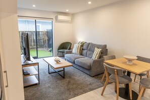 A modern living room with a grey sofa, a wooden coffee table, and a dining table with chairs. - Stylish Two-Bedroom Townhouse Near Lower Hutt (Lower Hutt)