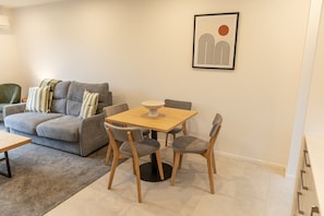 A modern living room with a grey sofa, a wooden dining table with four chairs, and a framed abstract artwork on the wall. - Stylish Two-Bedroom Townhouse Near Lower Hutt (Lower Hutt)