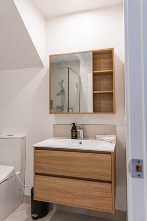 A modern bathroom with a white sink, wooden vanity, a mirror, and a shower enclosure. - Stylish Two-Bedroom Townhouse Near Lower Hutt (Lower Hutt)