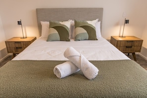 A neatly made bed with a green throw blanket, two pillows, and a rolled towel on a carpeted floor. - Stylish Two-Bedroom Townhouse Near Lower Hutt (Lower Hutt)