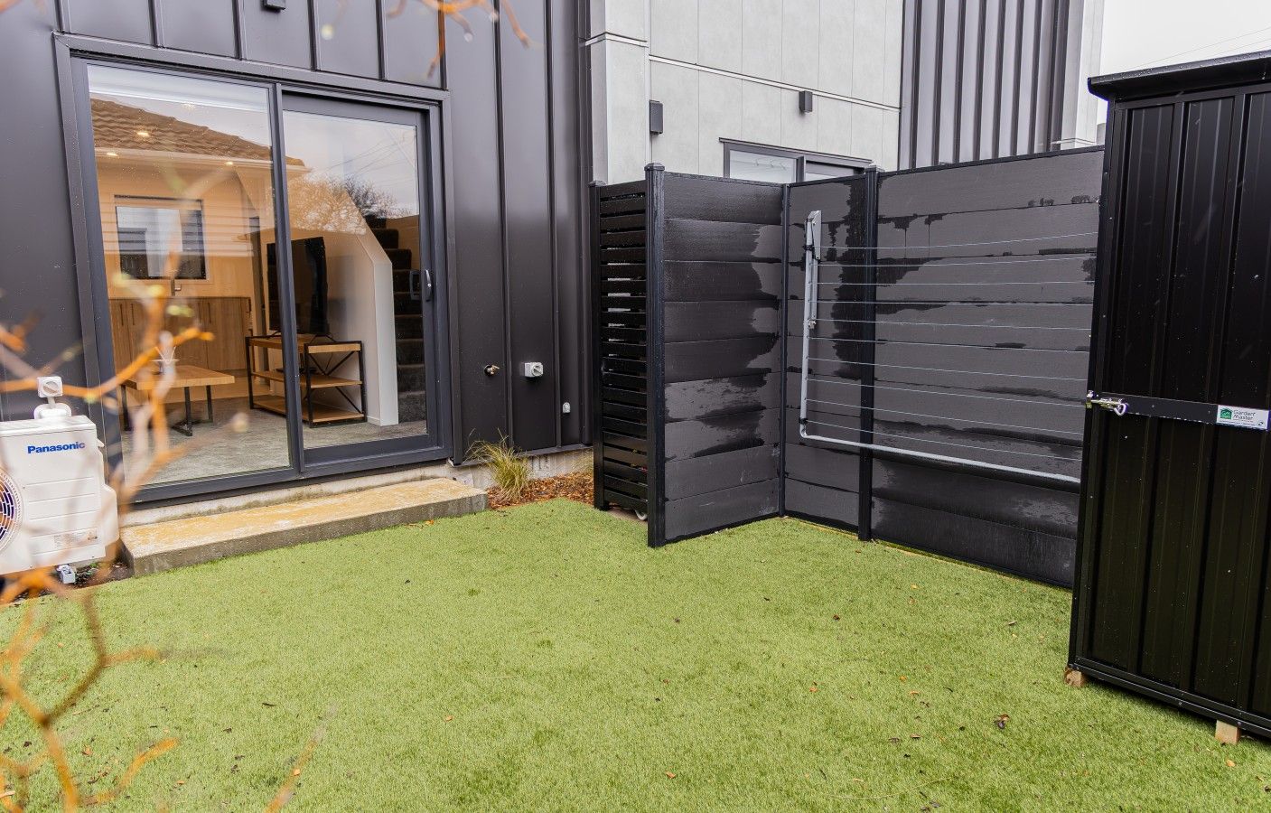 A modern building with a glass door entrance, a black metal fence, and artificial green grass.