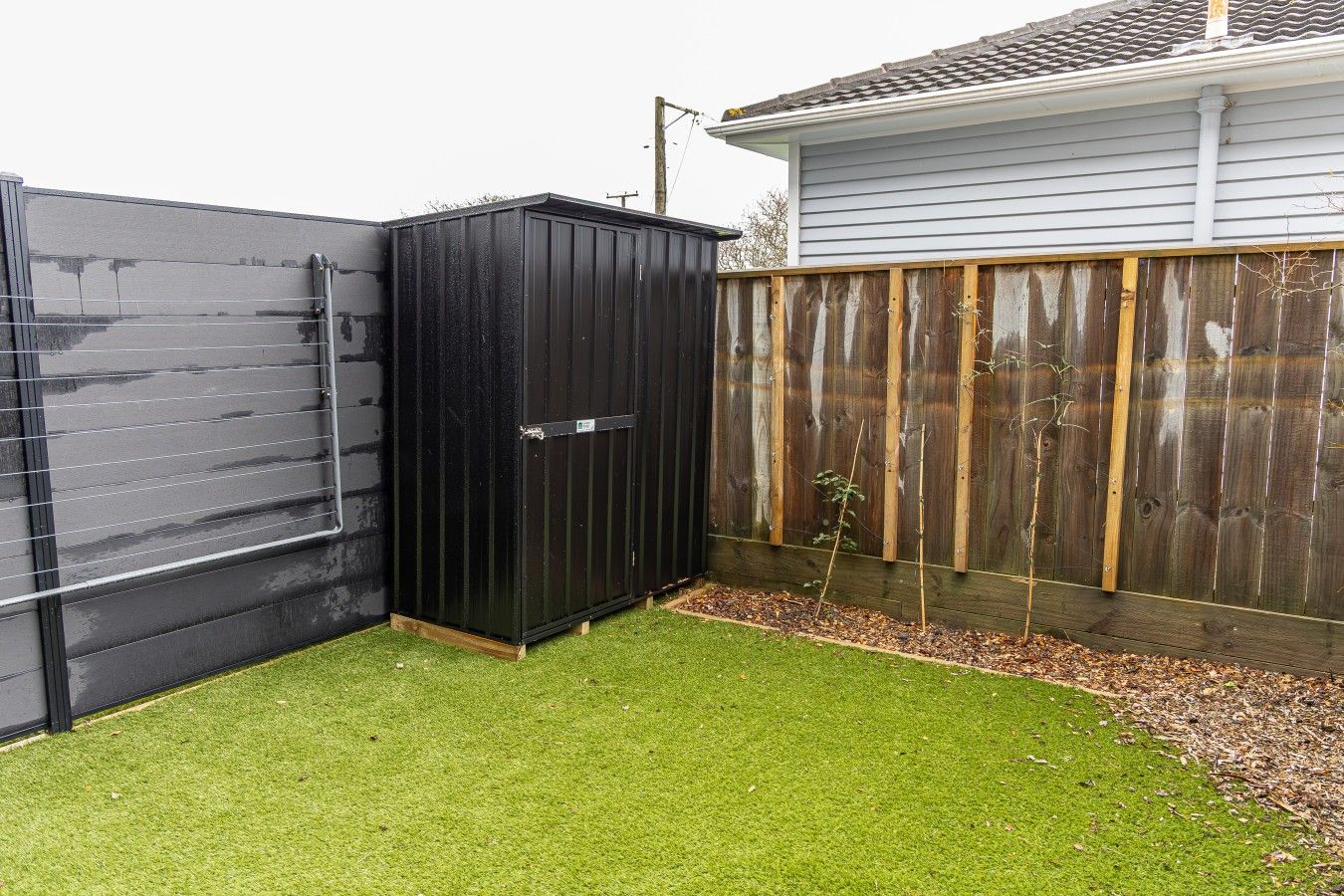 A fenced backyard with artificial grass, a black shed, and a wooden fence.