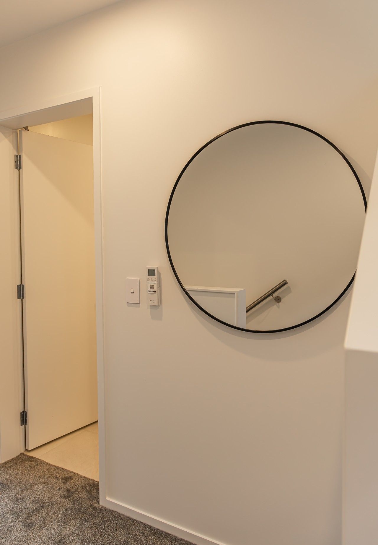 A room with a closed door, a wall-mounted circular mirror, and a thermostat on the wall.