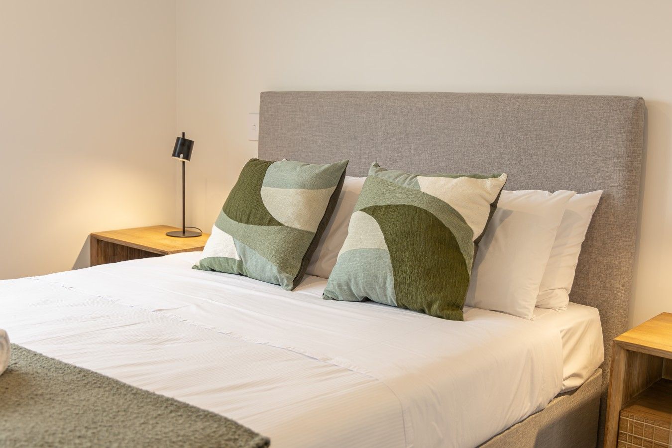 A bed with a grey headboard, two pillows, a bedside lamp, and a wooden nightstand.
