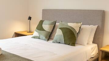 A bed with a grey headboard, two pillows, a bedside lamp, and a wooden nightstand.
