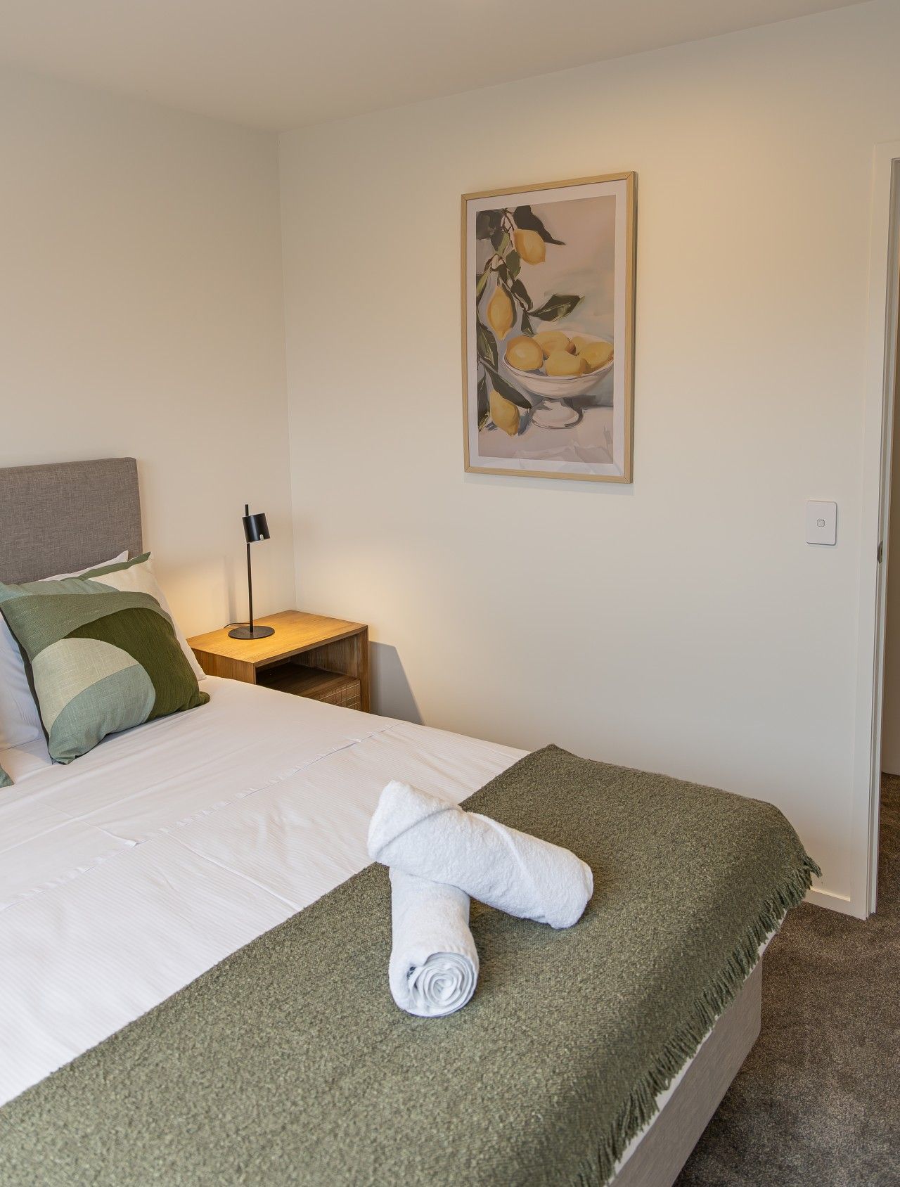 Een hotelkamer met een net opgemaakt bed, een nachtkastje met een lamp en een schilderij aan de muur.