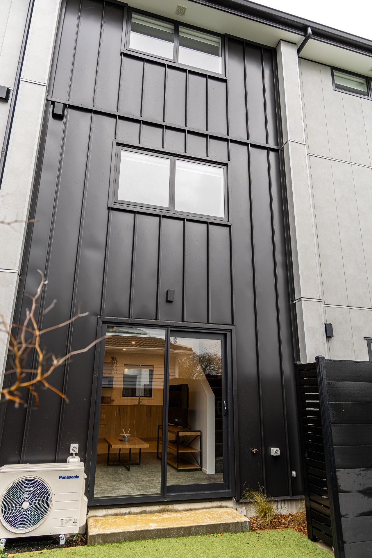 A modern building with a dark facade, large windows, and a visible interior with a dining area.