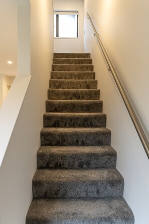 A carpeted staircase with a metal handrail, leading to a landing with a window.