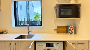 Cocina compacta con lavadora, microondas, lavabo y ventana con vista a edificios.