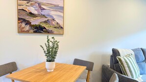 Un comedor con mesa de madera, cuatro sillas, una planta en maceta y un sofá con cojín a rayas.