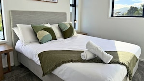 A neatly made bed with a white comforter, a green throw blanket, and a rolled towel. There is a framed picture on the wall above the bed. - Modern 1BR Townhouse with Private Courtyard (Lower Hutt)