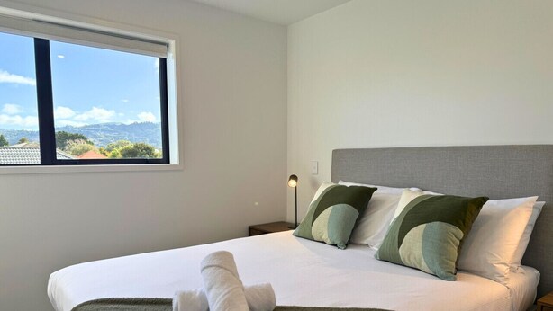 A neatly made bed with a green throw blanket, pillows, and a rolled towel. - Bright & Spacious Wellington Townhouse (Lower Hutt)