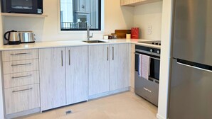 A modern kitchen with a stainless steel refrigerator, a microwave, a kettle, and a window above the sink. - Bright & Spacious Wellington Townhouse (Lower Hutt)