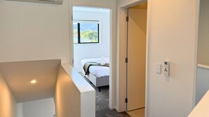 A modern hotel room with a bed, a window, an air conditioning unit, and a door leading to another room. - Bright & Spacious Wellington Townhouse (Lower Hutt)