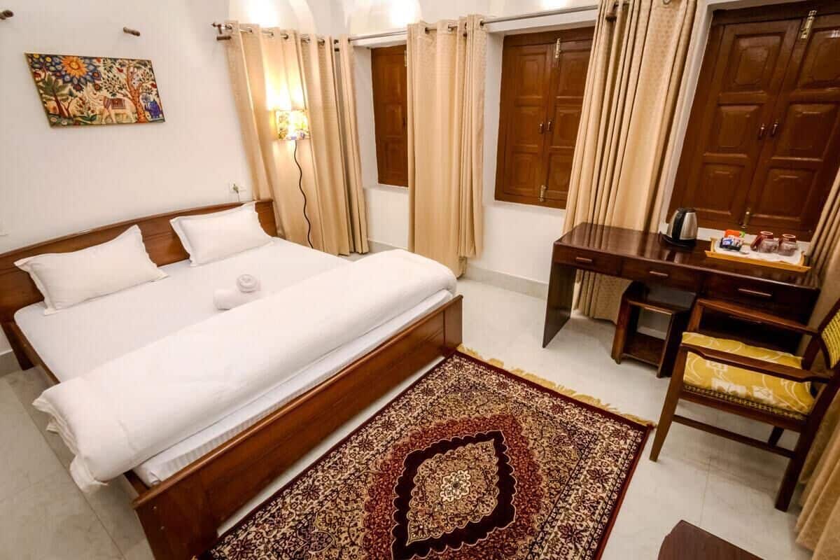 A hotel room with a bed, a desk, a chair, and a wooden wardrobe.