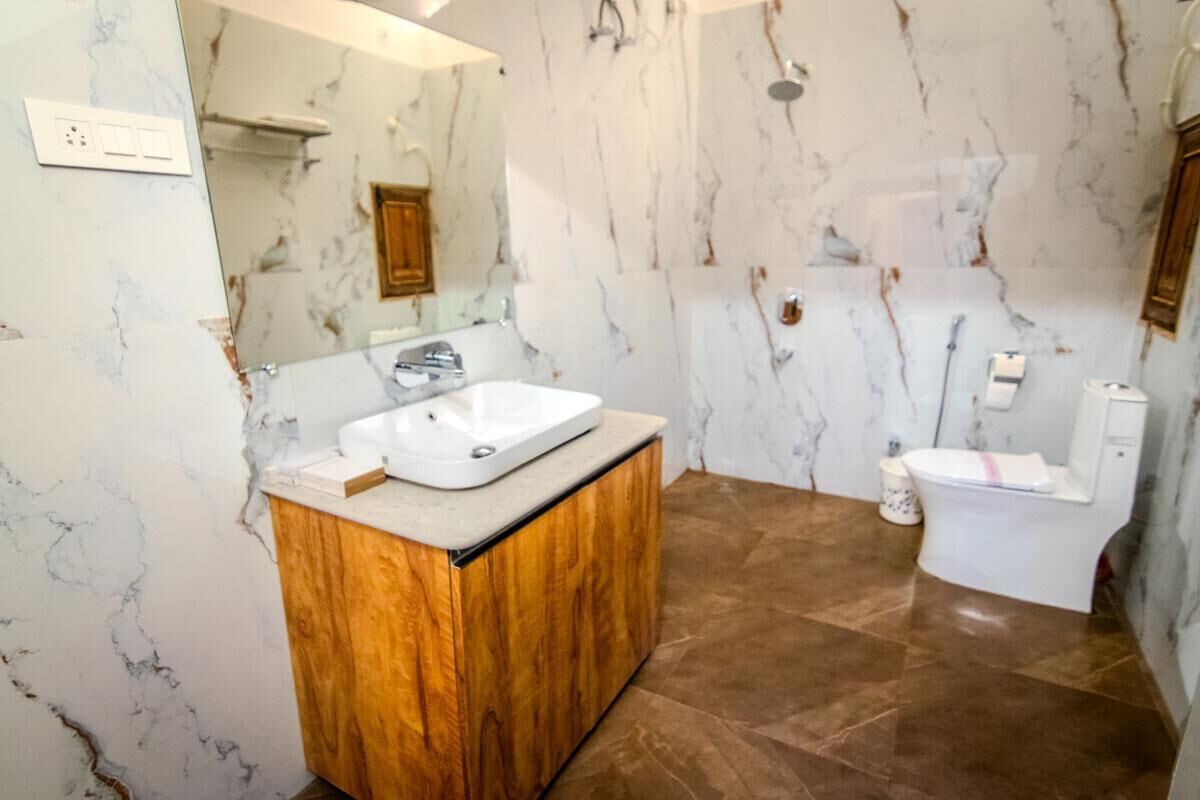 A bathroom with a marble wall, a wooden vanity, a white sink, a toilet, and a shower.